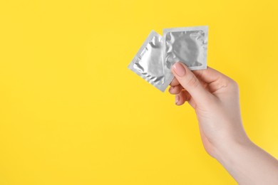 Photo of Woman holding condoms on yellow background, closeup. Space for text