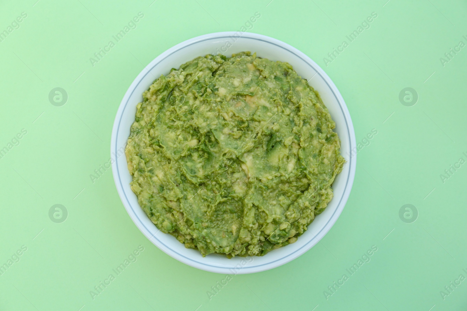 Photo of Delicious guacamole made of avocados on light green background, top view
