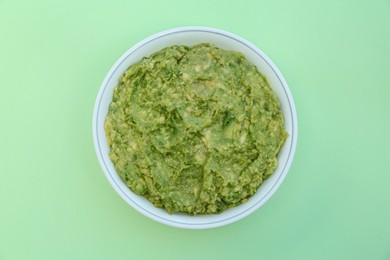 Photo of Delicious guacamole made of avocados on light green background, top view