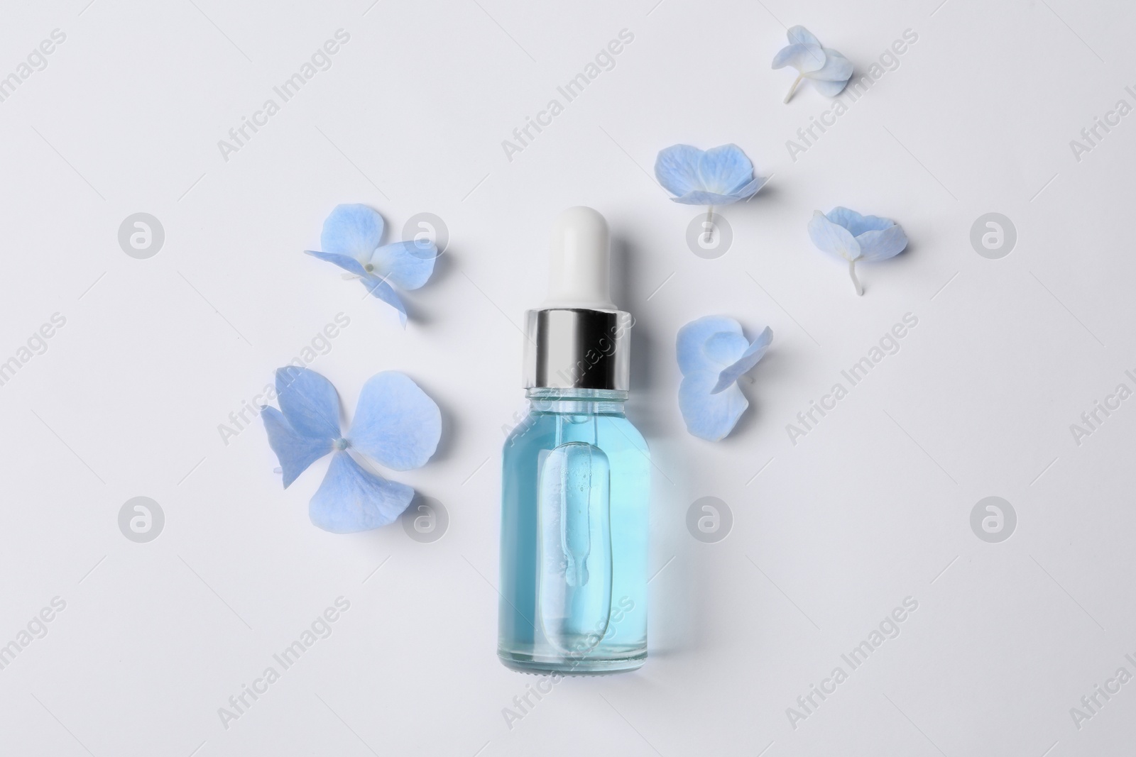 Photo of Bottle of cosmetic serum and beautiful flowers on white background, flat lay