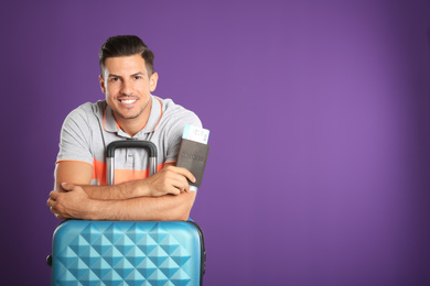 Photo of Handsome man with suitcase and ticket in passport for summer trip on purple background. Vacation travel