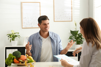 Photo of Young nutritionist consulting patient at table in clinic