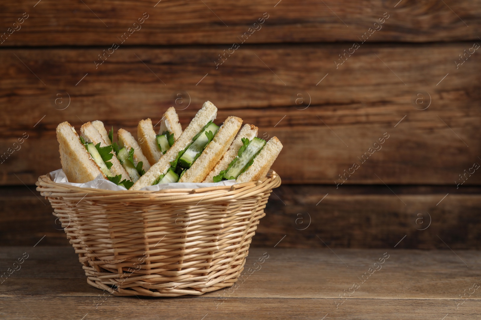 Photo of Tasty sandwiches with cucumber and parsley in wicker basket on wooden table. Space for text