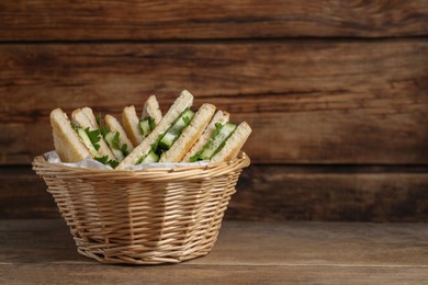 Tasty sandwiches with cucumber and parsley in wicker basket on wooden table. Space for text