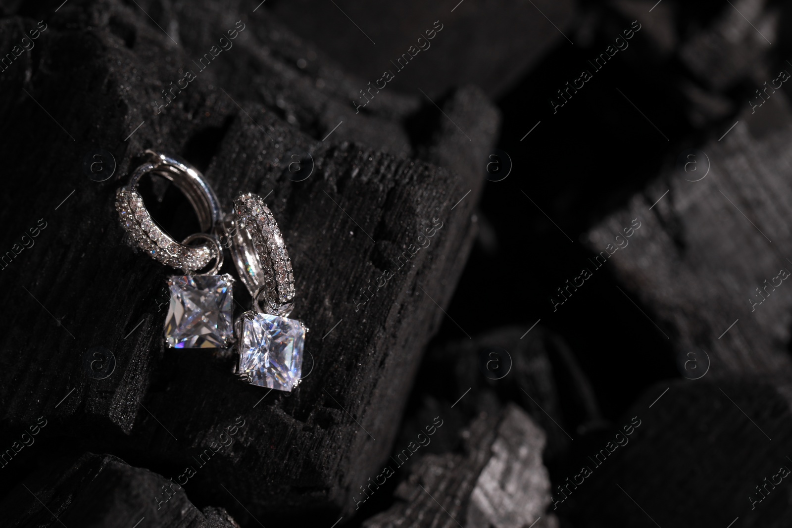 Photo of Luxury jewelry. Stylish presentation of elegant earrings on coal, closeup with space for text