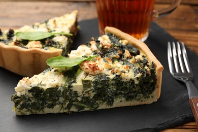 Photo of Pieces of delicious homemade spinach quiche on black board, closeup