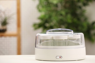 Modern yogurt maker with empty jars on white table indoors. Space for text