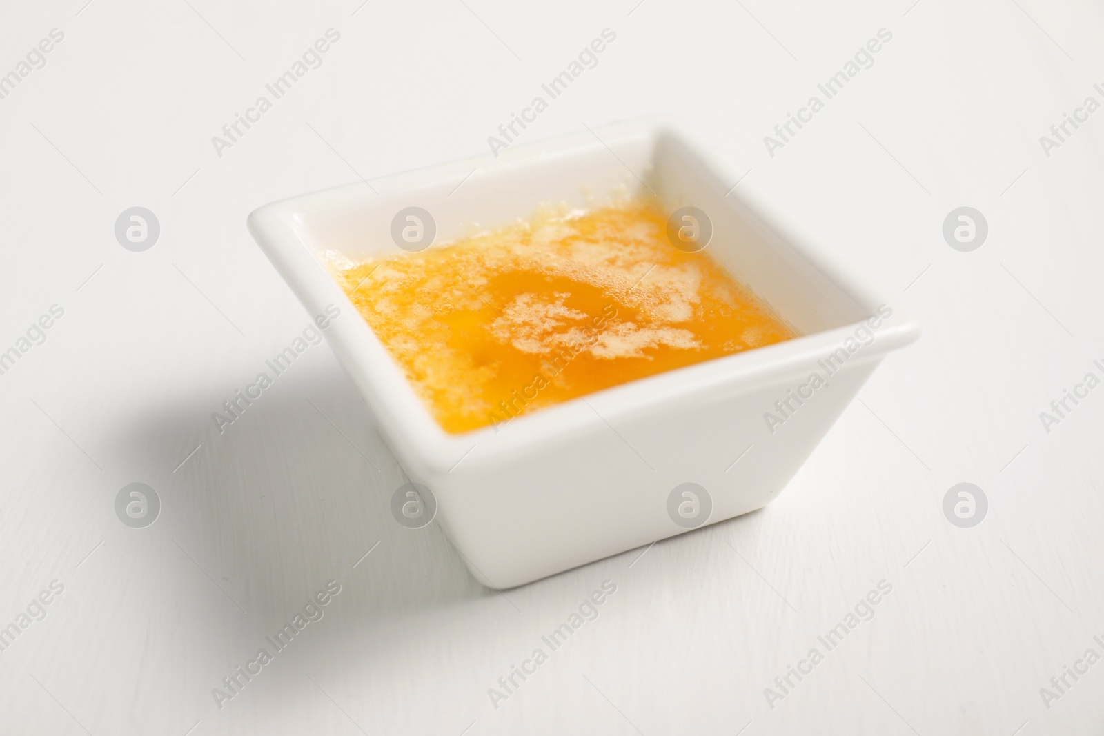 Photo of Melted butter in bowl on white wooden table, closeup