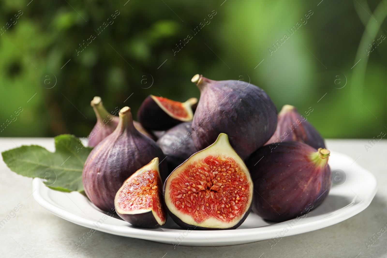 Photo of Whole and cut ripe figs on light table against blurred green background, closeup