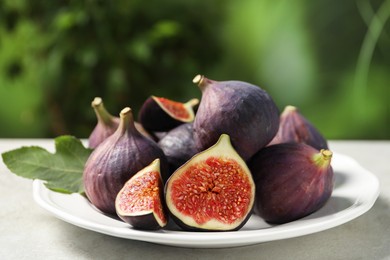 Photo of Whole and cut ripe figs on light table against blurred green background, closeup