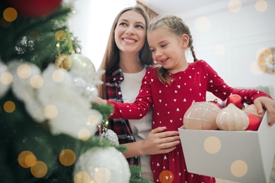Photo of Happy mother with her cute daughter decorating Christmas tree together at home
