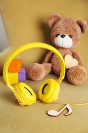 Baby songs. Headphones, wooden note, toy bear and cubes on armchair