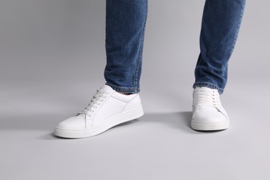 Man wearing stylish white sneakers on grey background, closeup