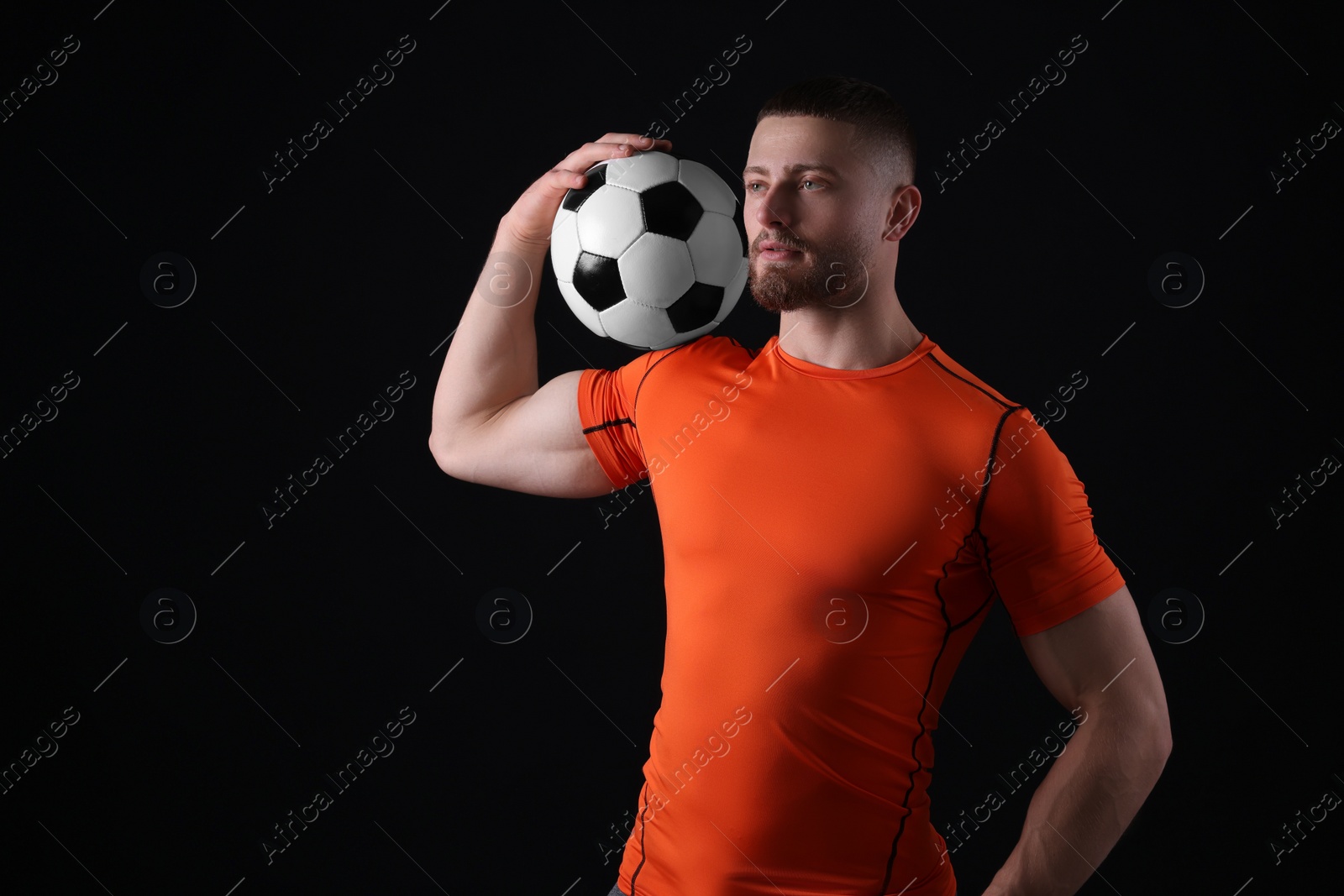 Photo of Athletic young man with soccer ball on black background