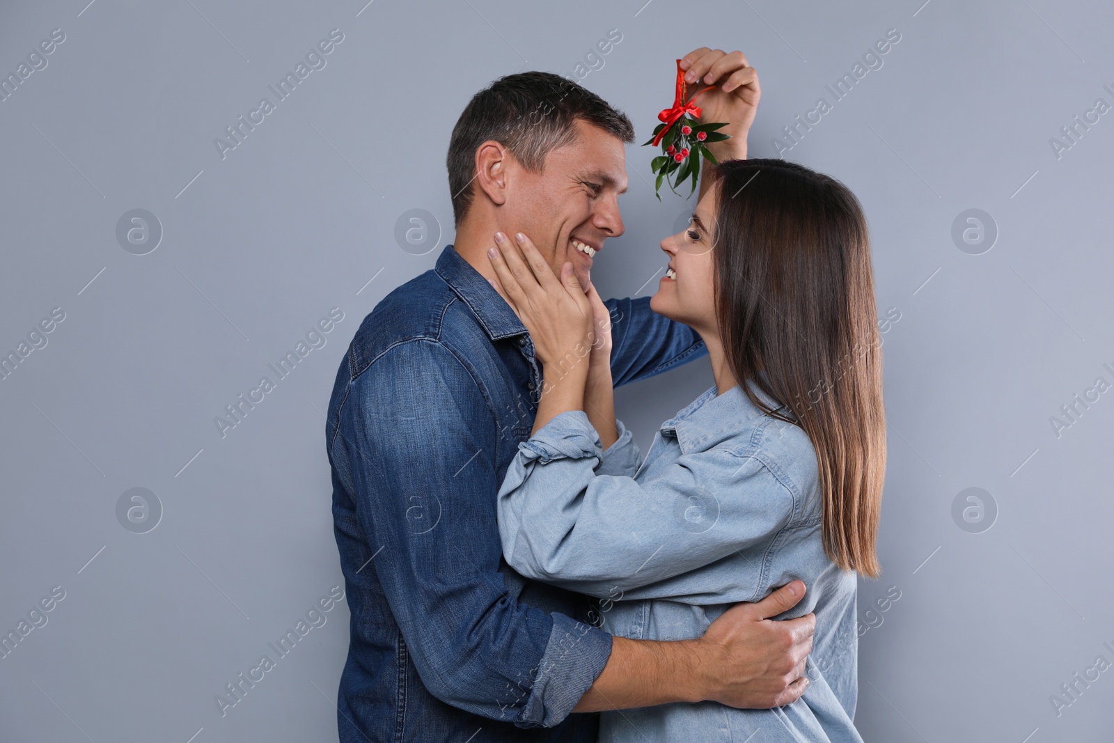 Photo of Happy couple standing under mistletoe bunch on grey background