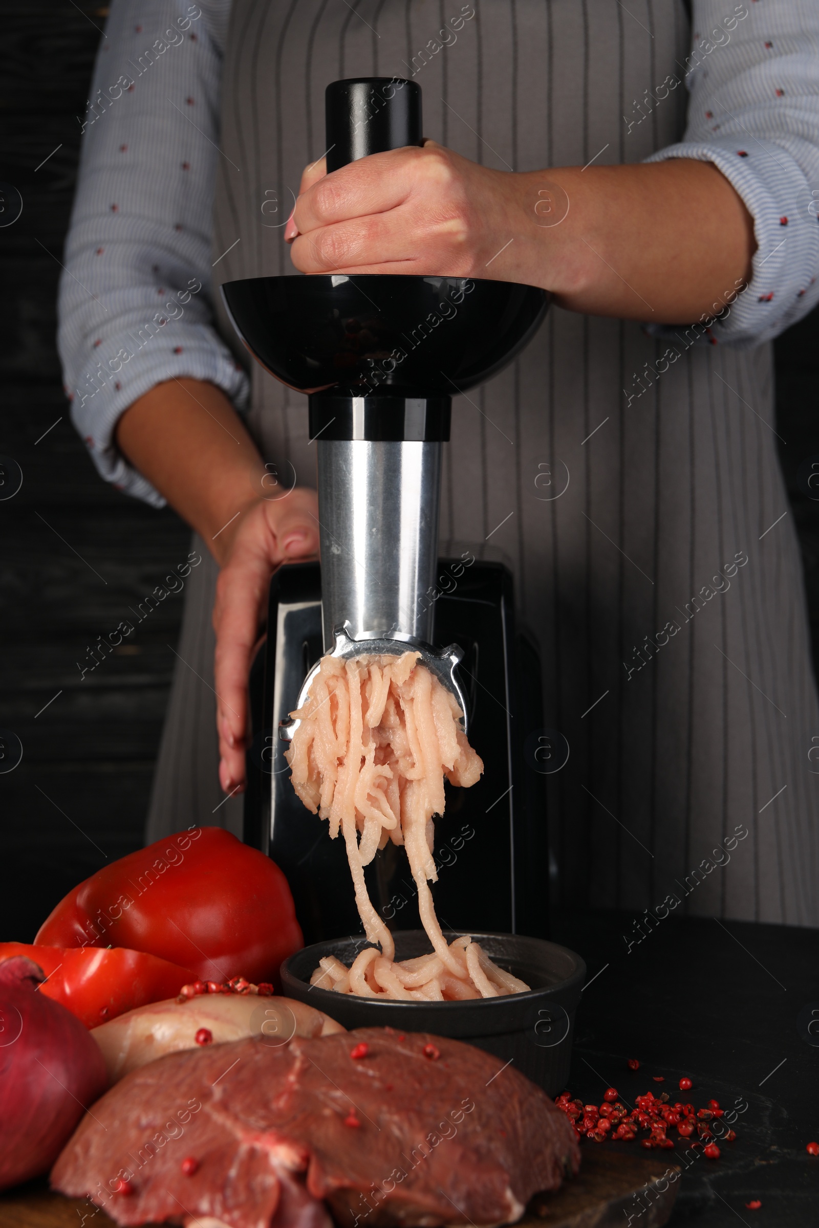 Photo of Woman making chicken mince with electric meat grinder at black table, closeup