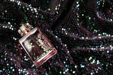 Luxury perfume in bottle on fabric with colorful sequins, above view