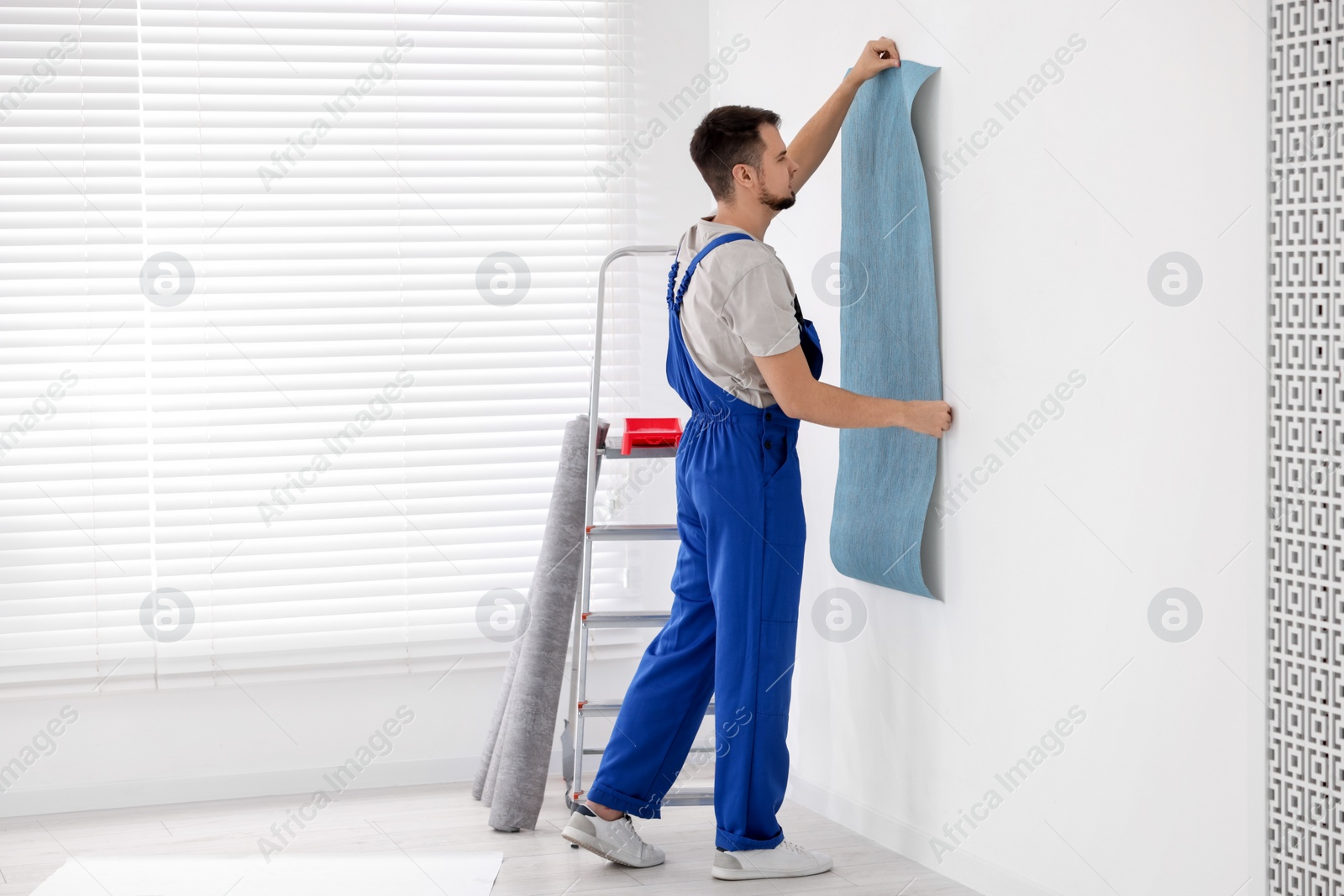 Photo of Man hanging light blue wallpaper in room