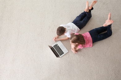 Photo of Teenage girl and her brother with laptop lying on cozy carpet at home