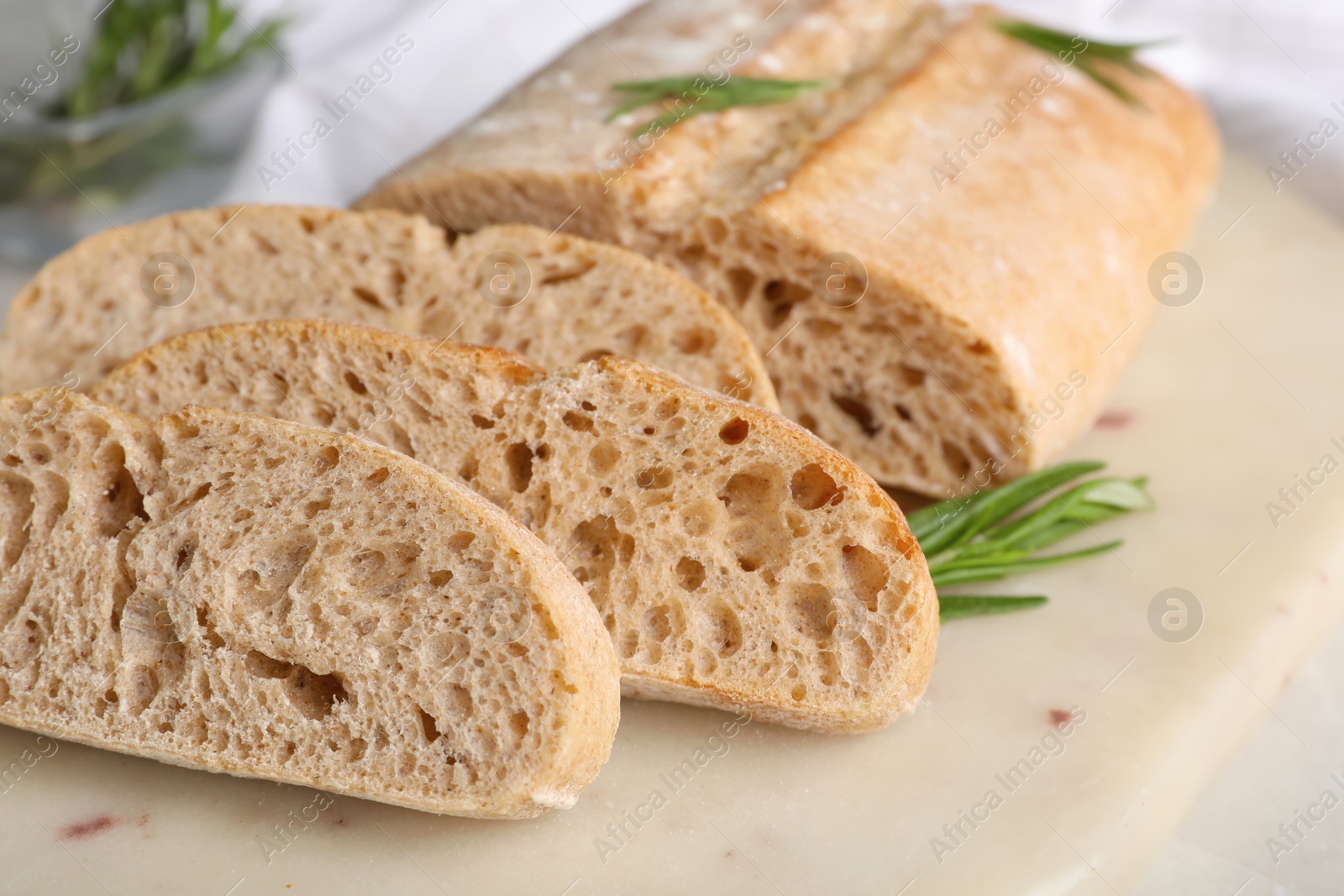 Photo of Cut delicious ciabatta with rosemary on white board, closeup