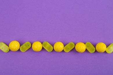 Photo of Delicious lemon candies on purple background, flat lay