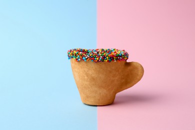 Photo of Delicious edible biscuit coffee cup decorated with sprinkles on color background