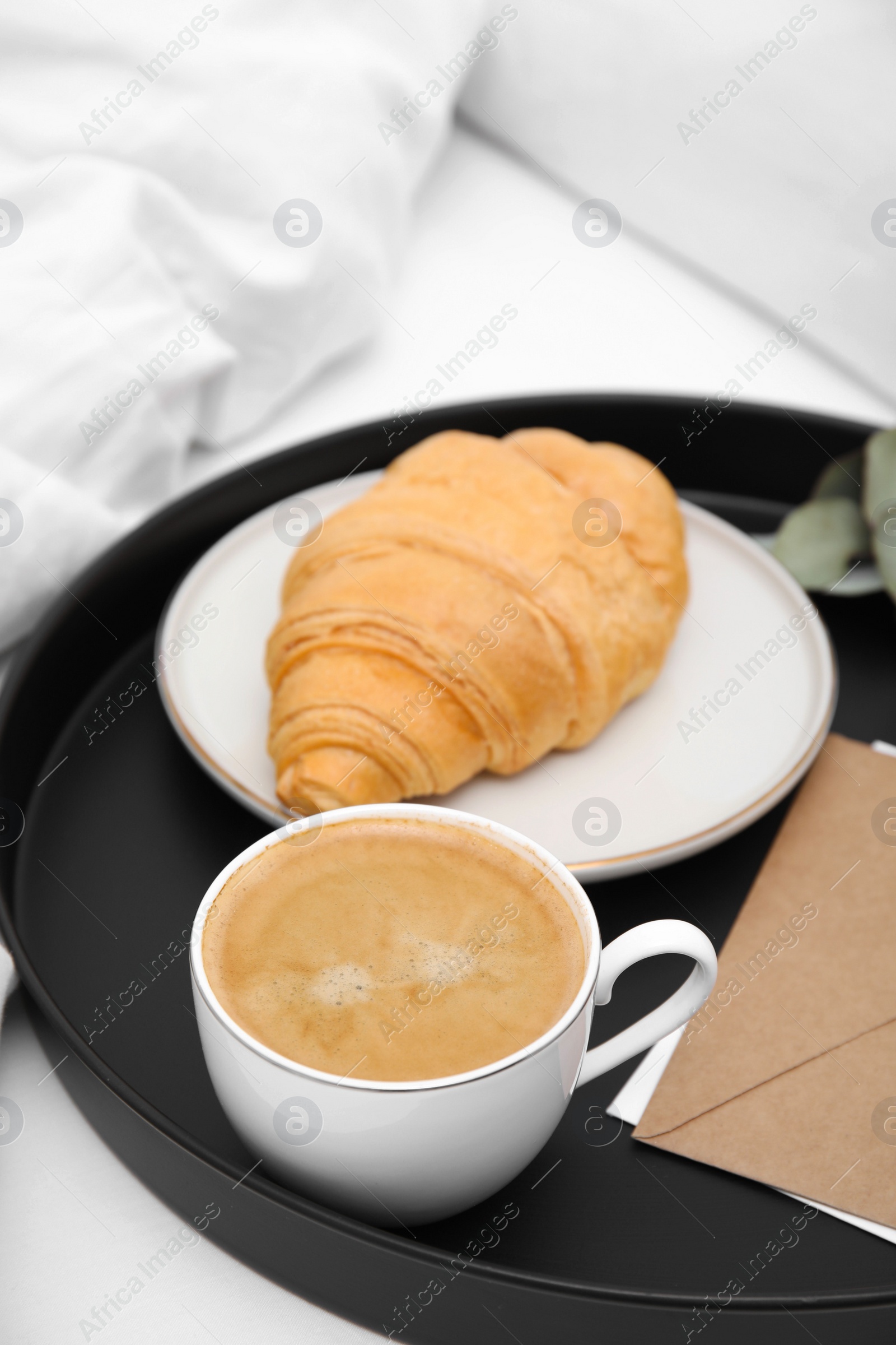 Photo of Tray with tasty croissant, cup of coffee and envelope on white bed