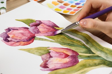 Woman painting tulips in sketchbook at table, closeup