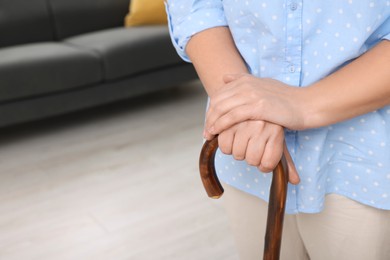 Photo of Senior woman with walking cane at home, closeup. Space for text