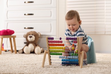 Little child with abacus sitting on plastic baby potty indoors. Space for text