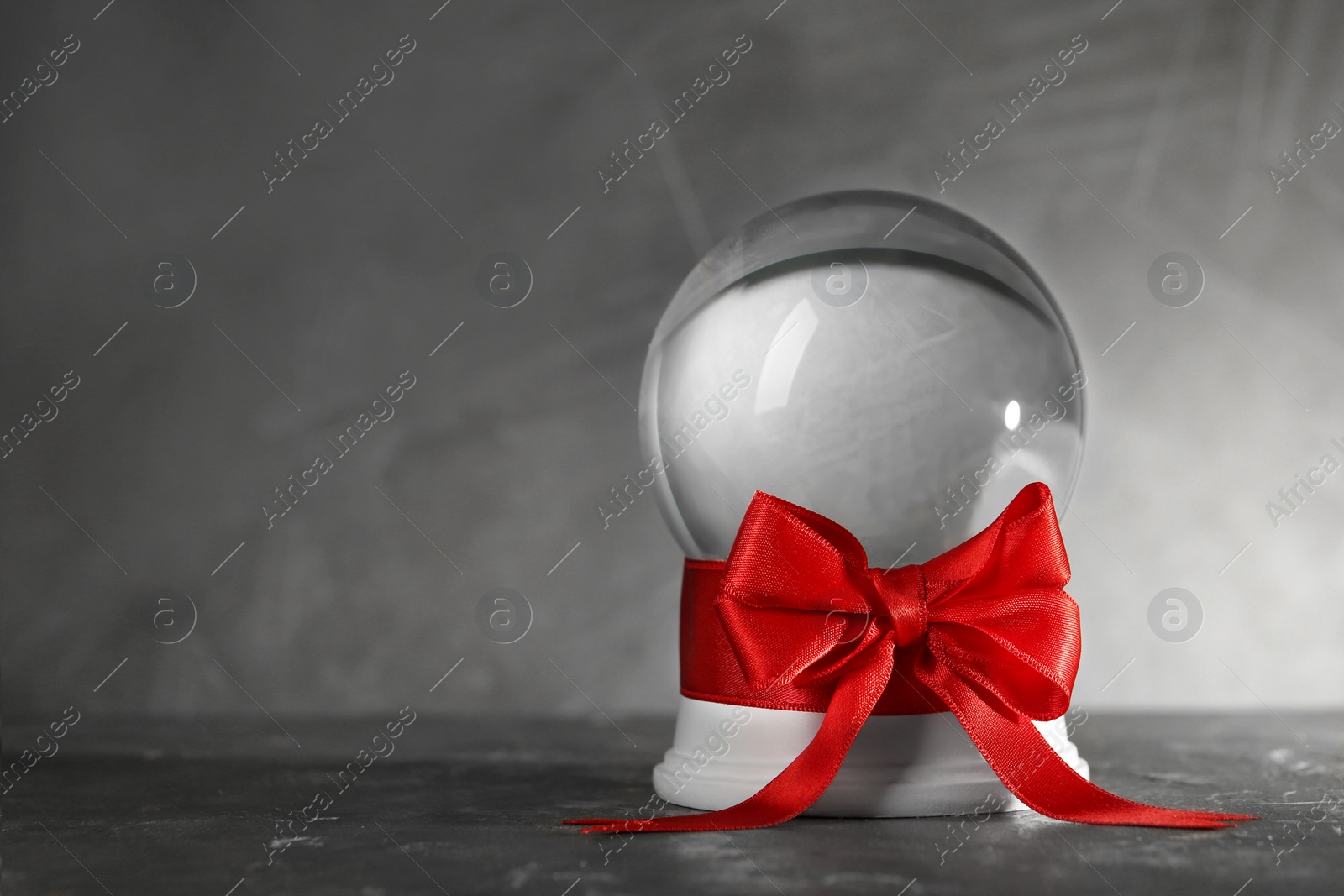 Photo of Beautiful Christmas snow globe with red bow on grey table, space for text