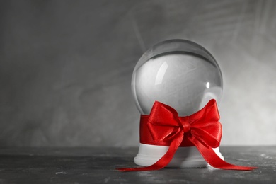 Beautiful Christmas snow globe with red bow on grey table, space for text