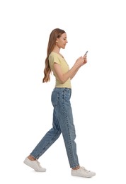 Young woman in casual outfit using smartphone while walking on white background