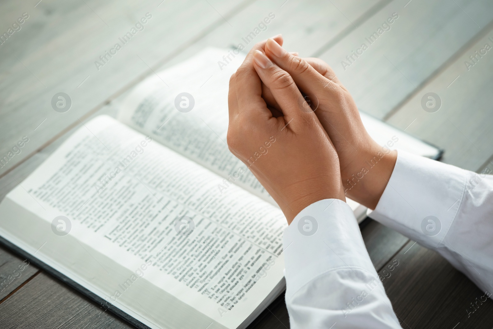 Photo of Woman holding hands clasped while praying at grey wooden table with Bible, closeup