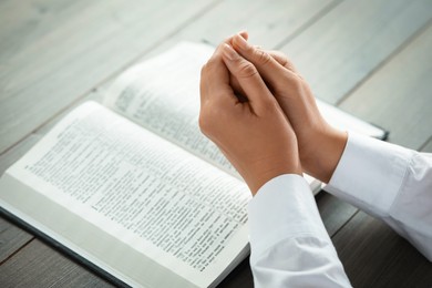 Photo of Woman holding hands clasped while praying at grey wooden table with Bible, closeup