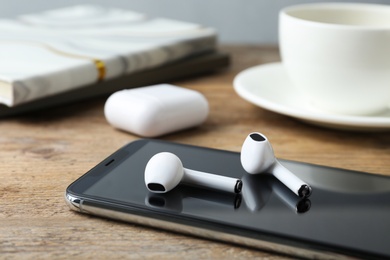 Photo of Modern wireless earphones and mobile phone on wooden table