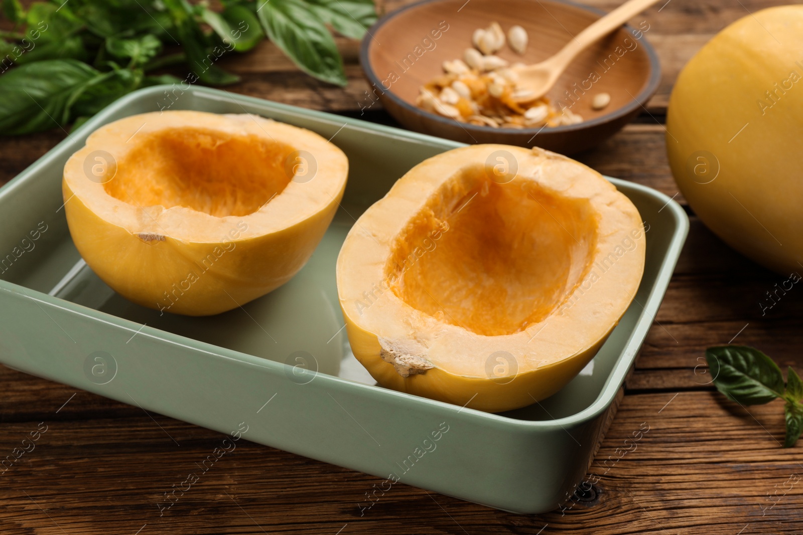 Photo of Halves of fresh spaghetti squash in baking dish on wooden table. Cooking at home