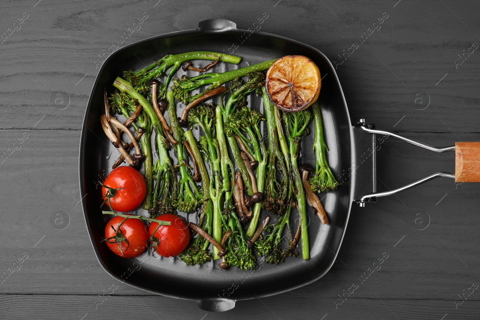 Photo of Grill pan with tasty cooked broccolini, mushrooms, tomatoes and lemon on grey wooden table, top view