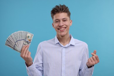 Photo of Happy man with dollar banknotes showing money gesture on light blue background