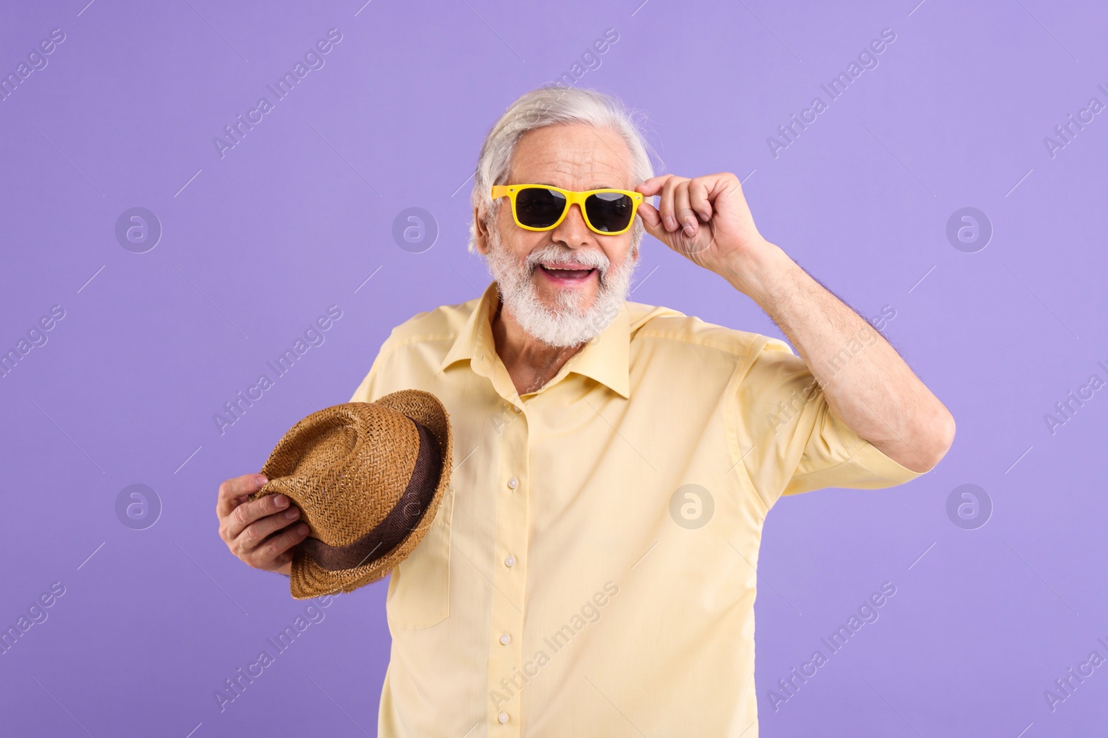 Photo of Portrait of stylish grandpa with sunglasses and hat on purple background