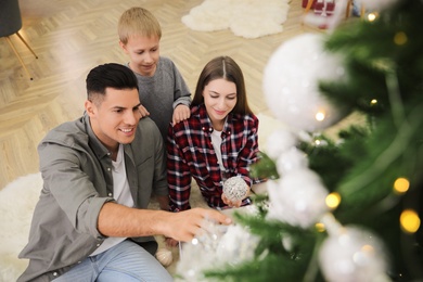 Happy family with cute child decorating Christmas tree together at home