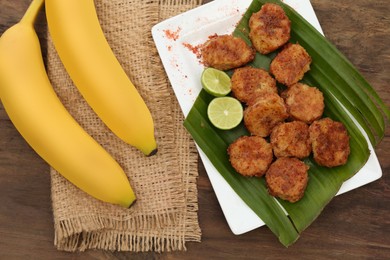 Delicious fried bananas, fresh fruits and cut limes on wooden table, flat lay