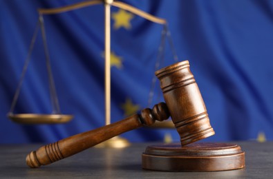 Photo of Wooden judge's gavel and Scales of justice on grey table against European Union flag