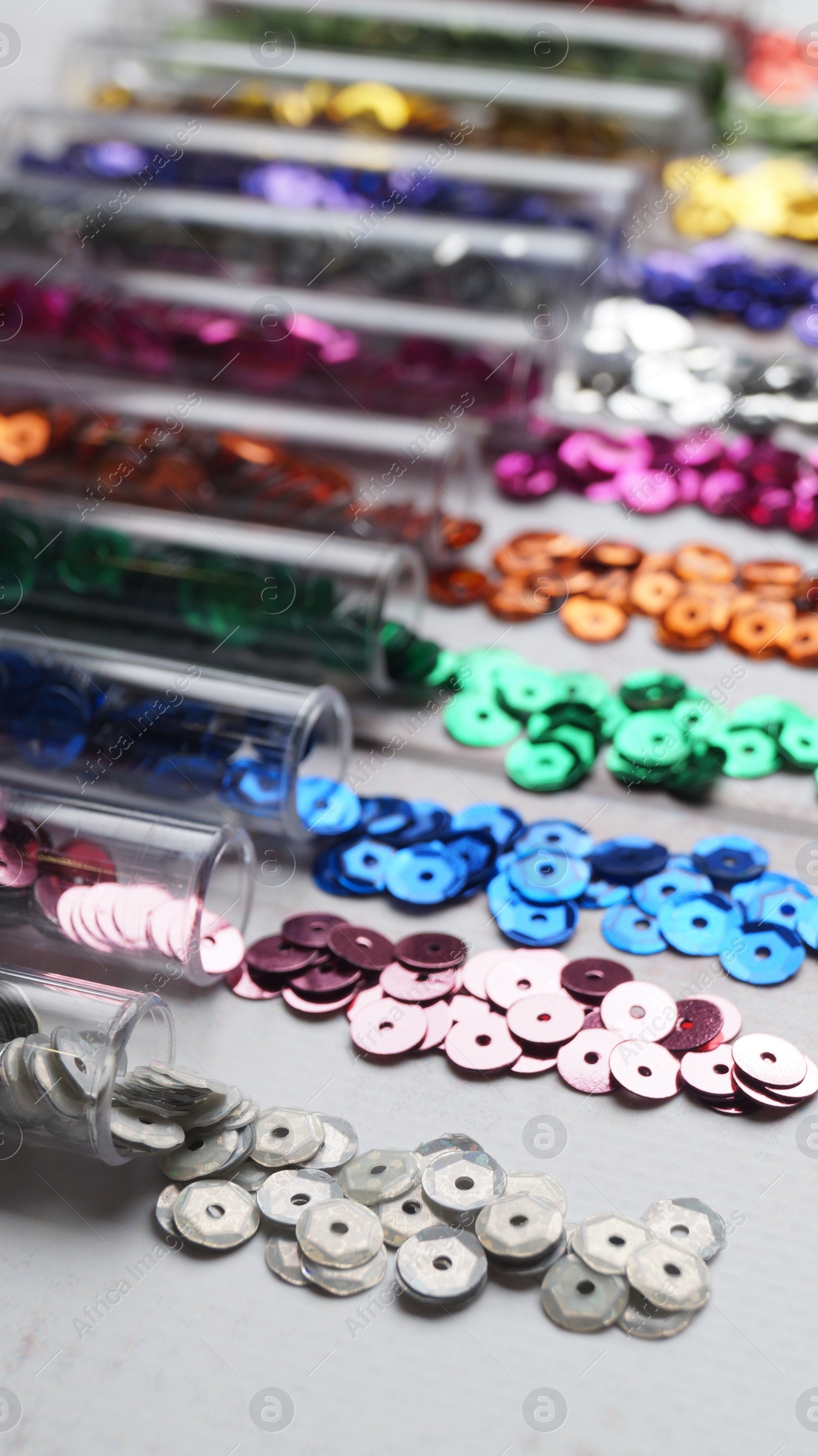 Photo of Tubes with many colorful sequins on white wooden table, closeup