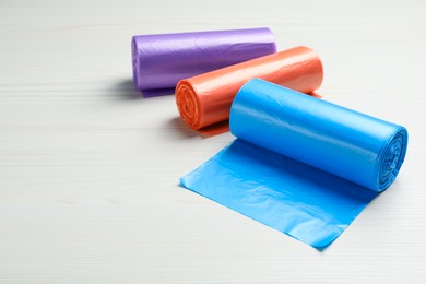 Photo of Rolls of different color garbage bags on white wooden table. Space for text