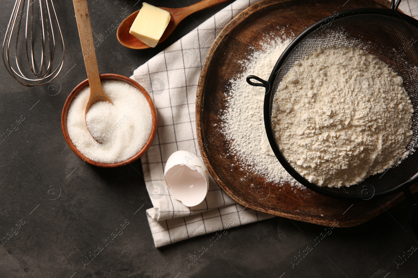 Photo of Making dough. Flour in sieve, sugar and butter on grey textured table, flat lay