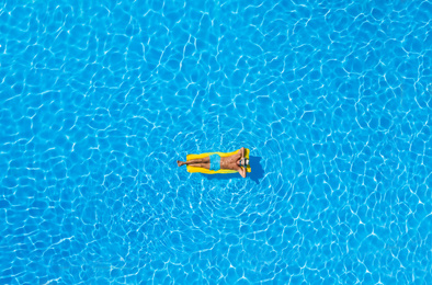 Young man with inflatable mattress in swimming pool, top view. Summer vacation