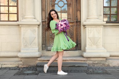 Photo of Beautiful woman with bouquet of spring flowers near building outdoors