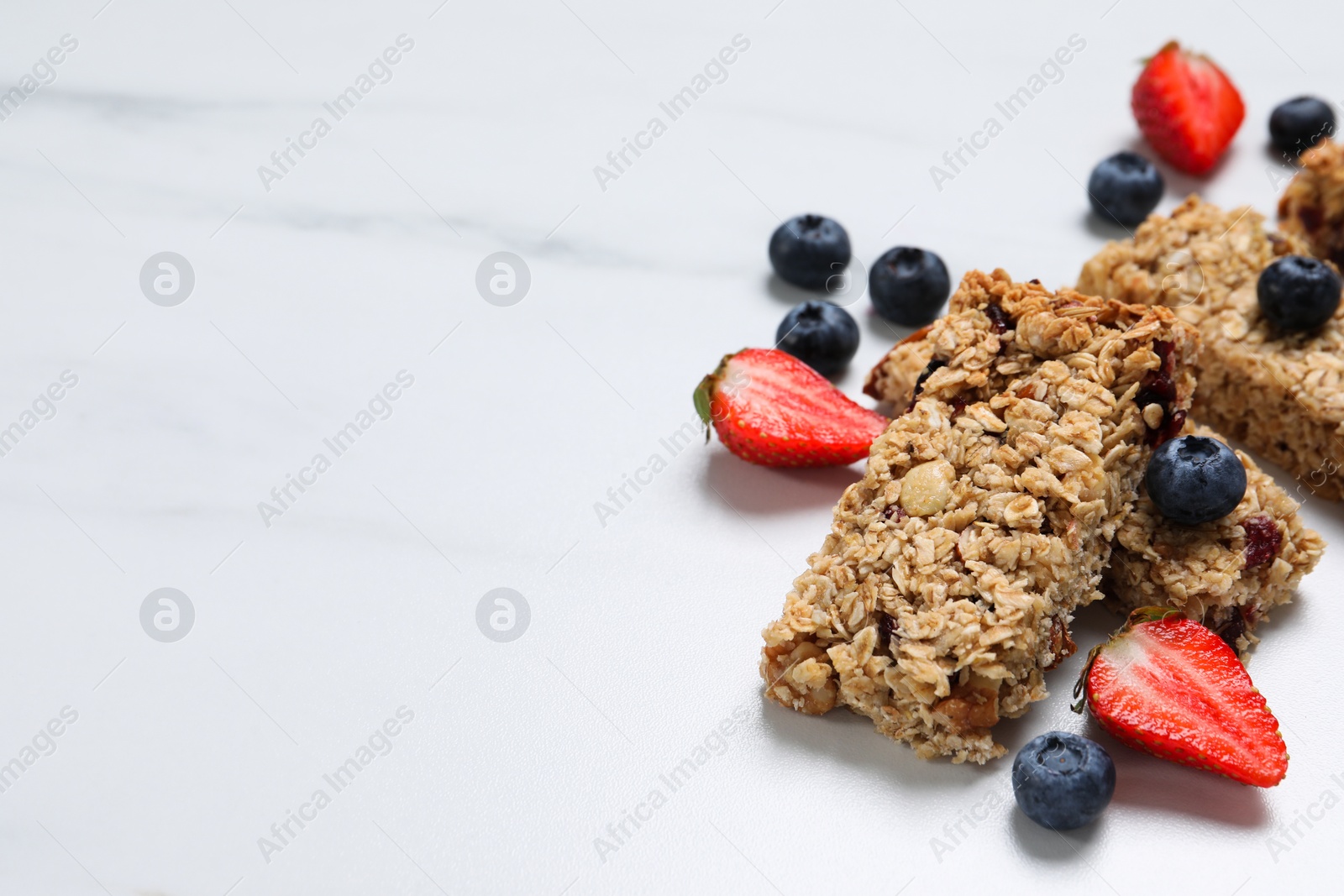 Photo of Tasty granola bars and berries on white marble table. Space for text