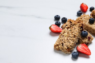 Tasty granola bars and berries on white marble table. Space for text